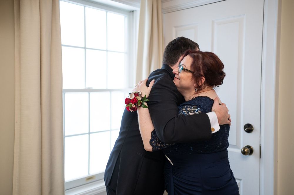 A couple embraces in a sunlit room with white curtains and windows during an intimate moment.