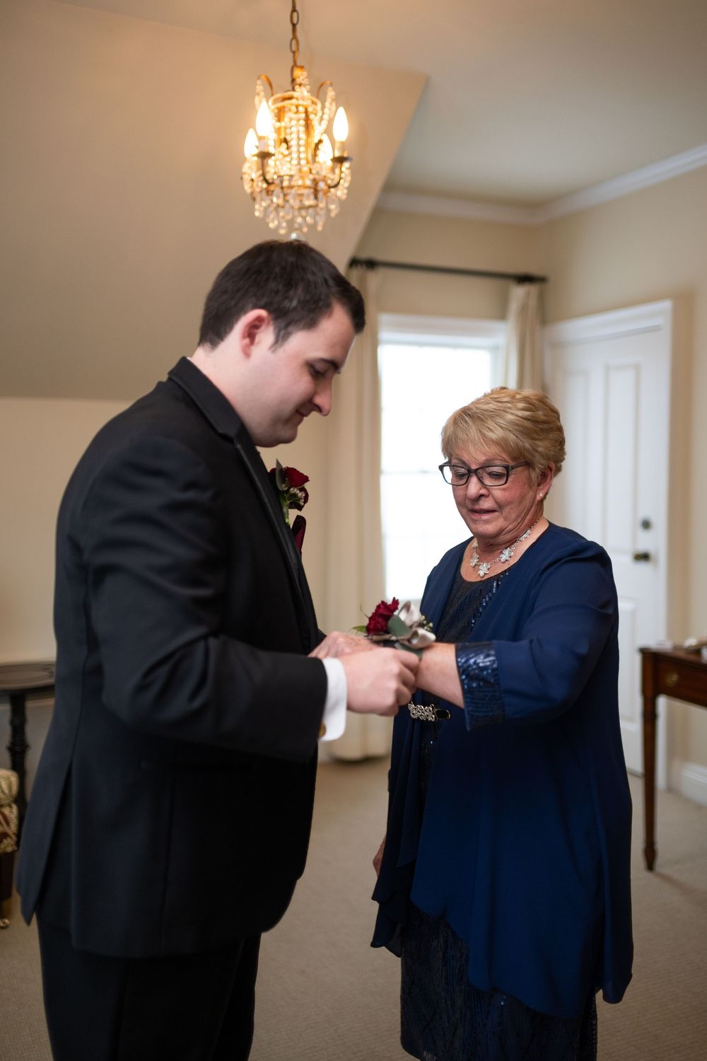 Person in a black suit having their boutonniere pinned on by someone in navy blue.