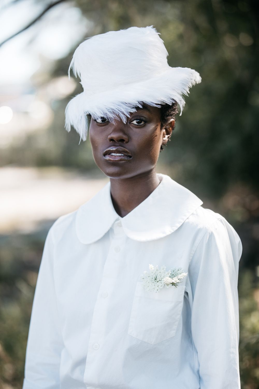 Series of artistic portraits featuring someone in an all-white outfit with feathered accessories in natural lighting.