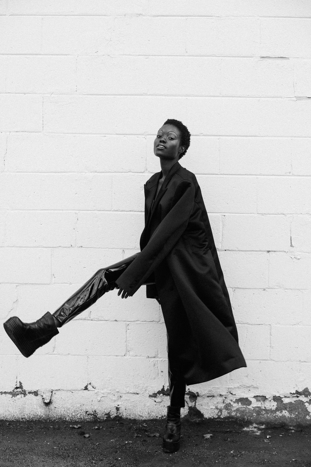 Artistic black and white fashion series showing dynamic poses against a white brick wall.