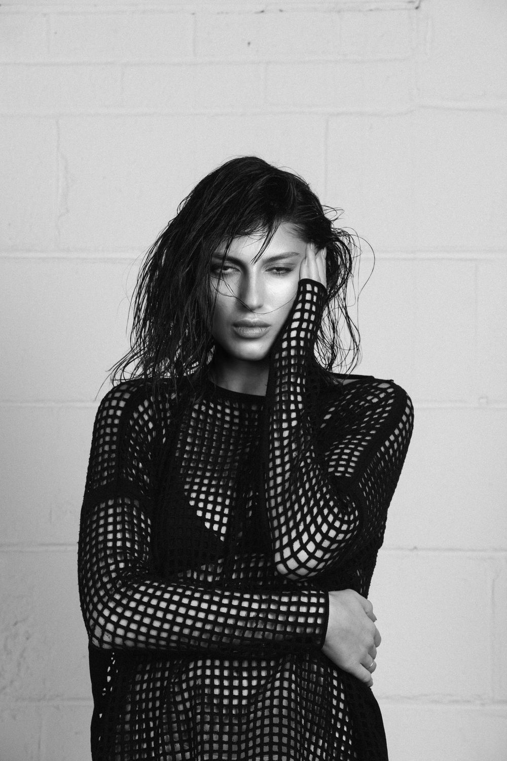 Black and white portrait series showing a person in a mesh top striking different dramatic poses against a white wall.