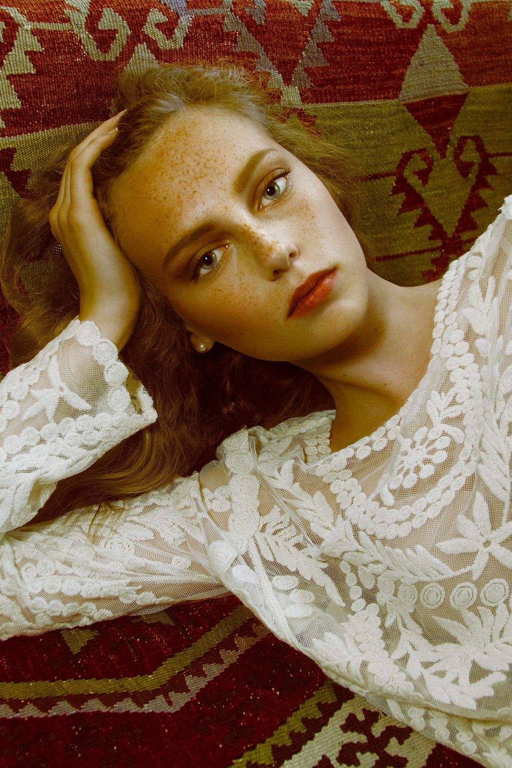 A series of artistic fashion portraits showing a person lying on a patterned rug wearing delicate white lace.