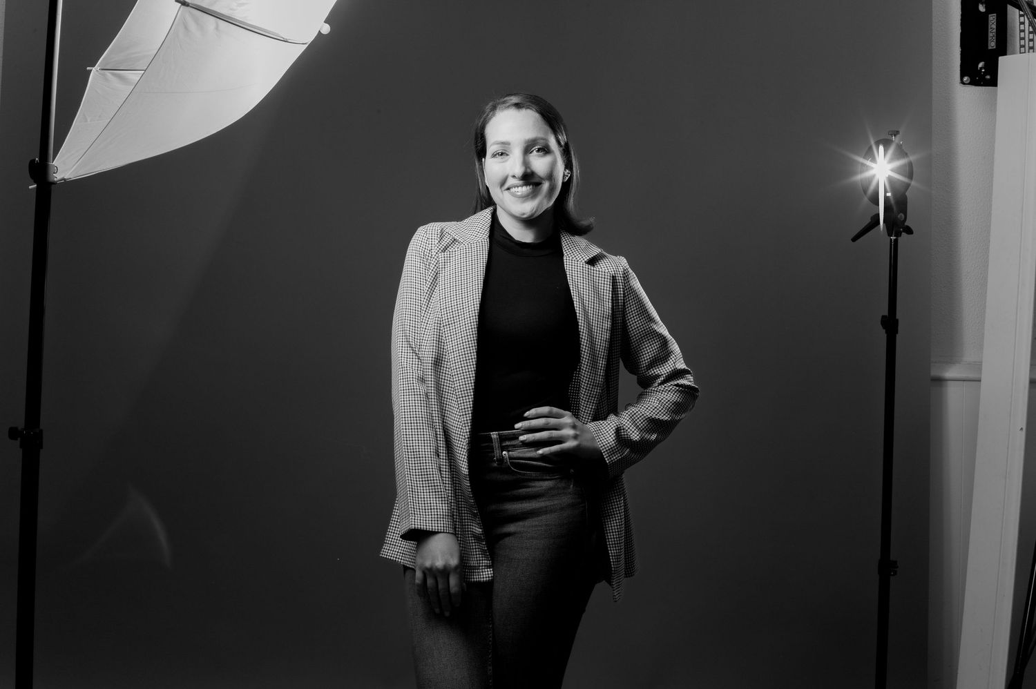 Black and white studio photograph showing a person smiling in a light blazer and dark top with professional lighting setup.