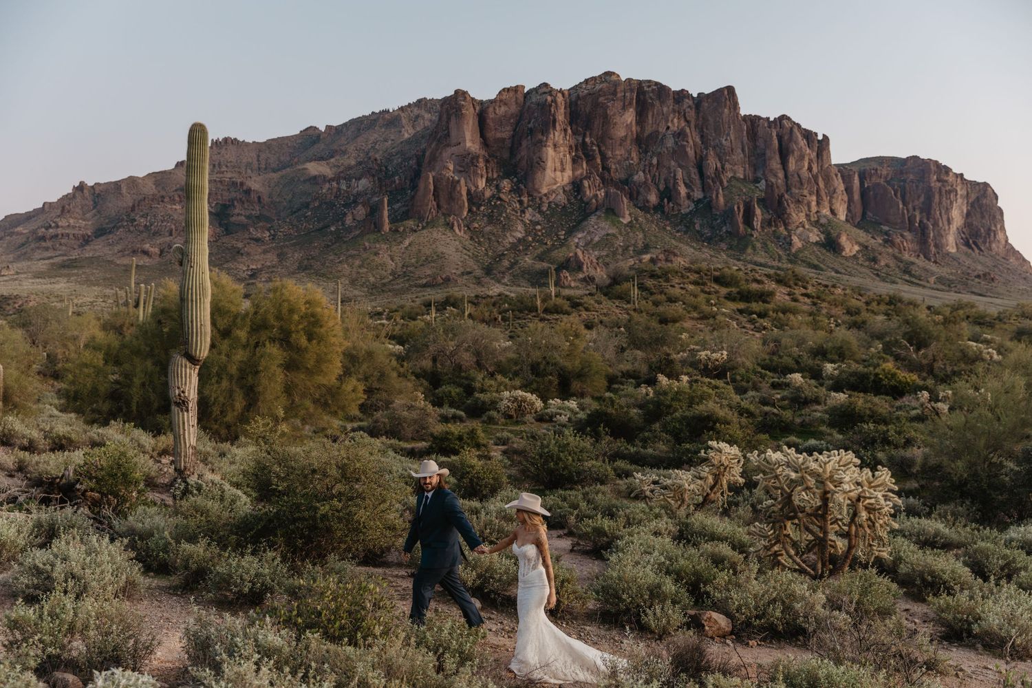 Elegant outdoor wedding reception at a Southwestern venue with white linens, floral centerpieces, ghost chairs, and string lights.
