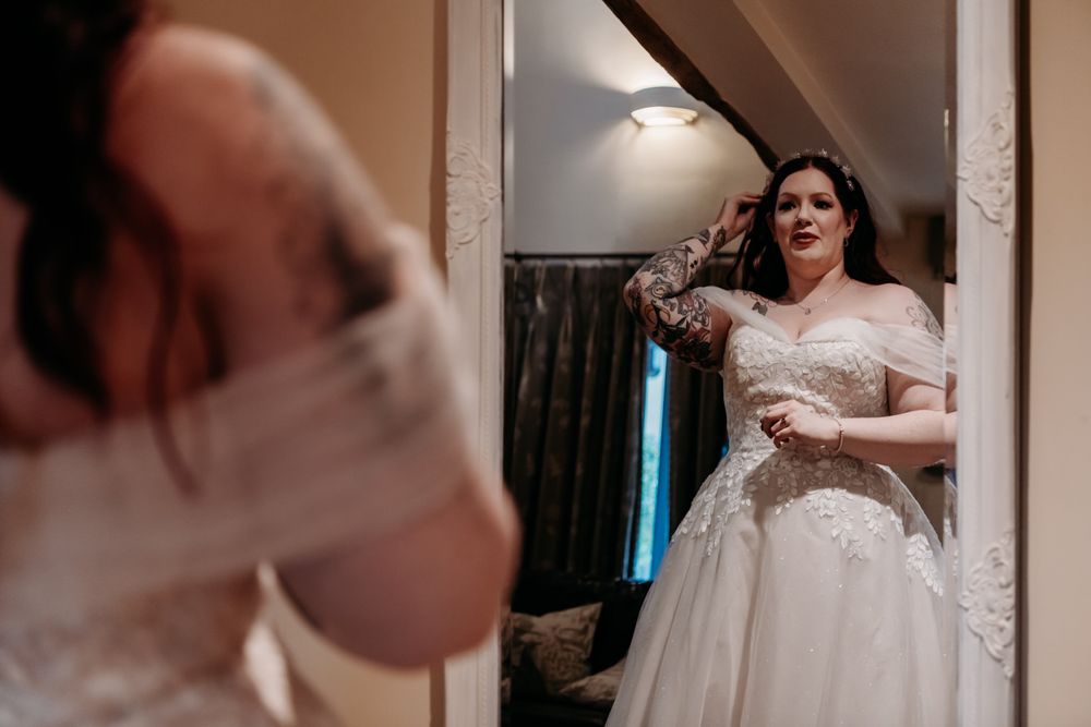 A bride in a flowing white wedding dress adjusts her veil while getting ready in a softly lit dressing room.