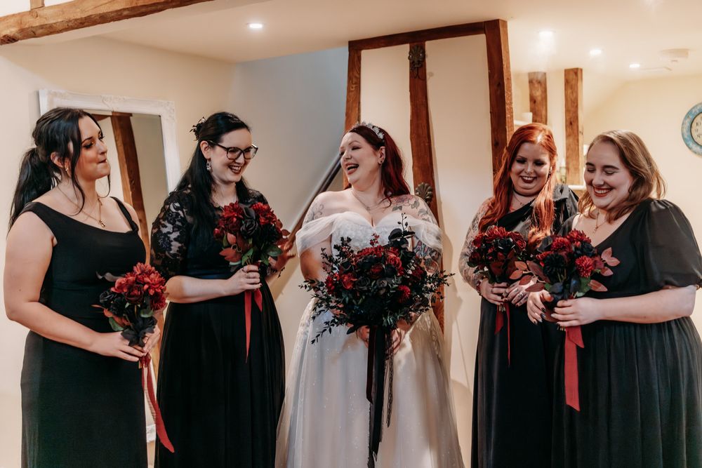 A bridal party wearing dark green dresses holds vibrant red bouquets while gathered together for a wedding photo.