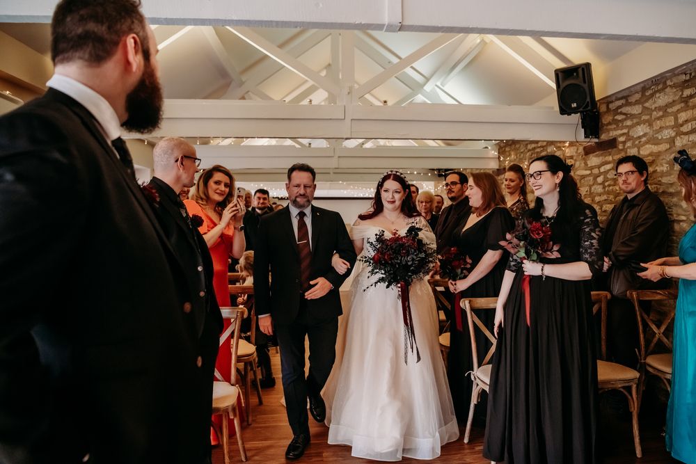 Wedding guests gather in an elegant venue with exposed brick walls and white beamed ceiling during a celebration.