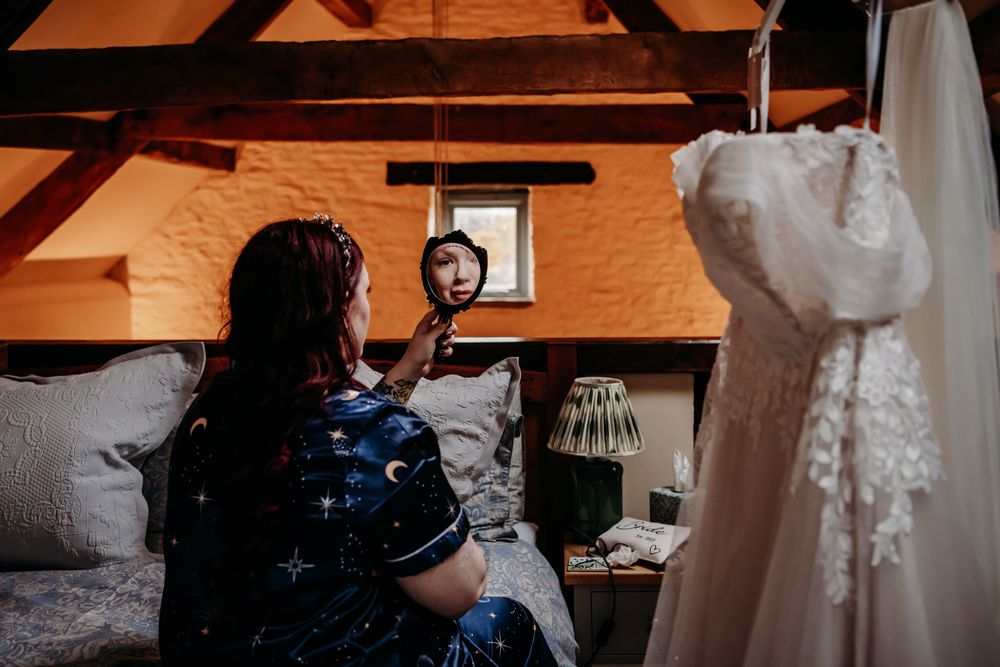 A person works on a detailed wedding dress in a sunlit sewing studio with wooden beams and warm lighting.