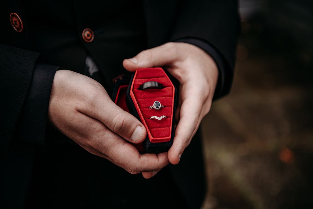 A sequence of hands opening a small red ring box to reveal a diamond engagement ring inside.