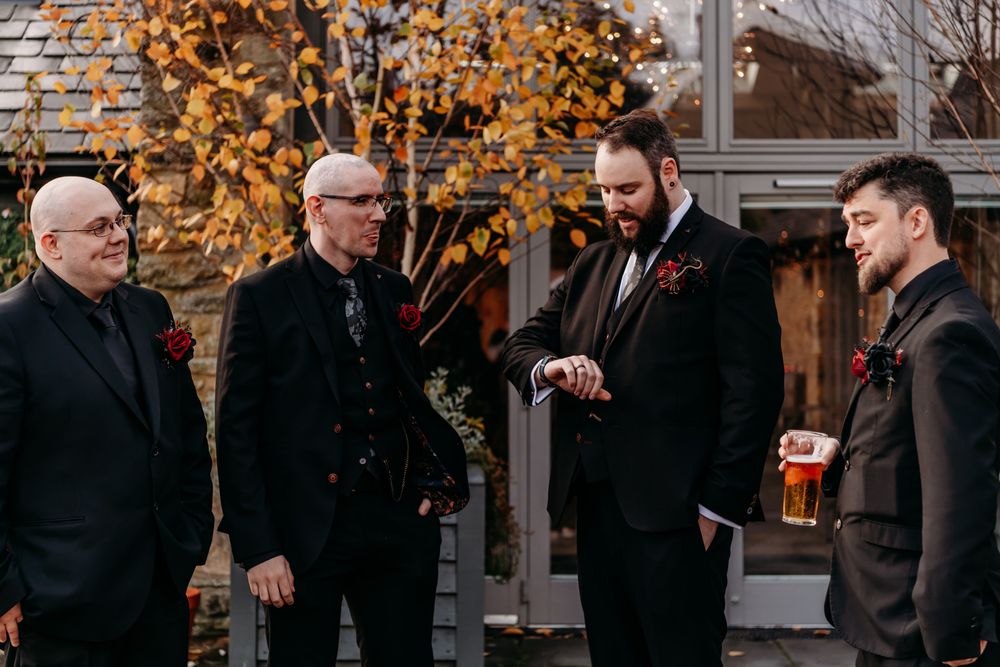 A group of men in black coats stand together talking and laughing during a social gathering outdoors.