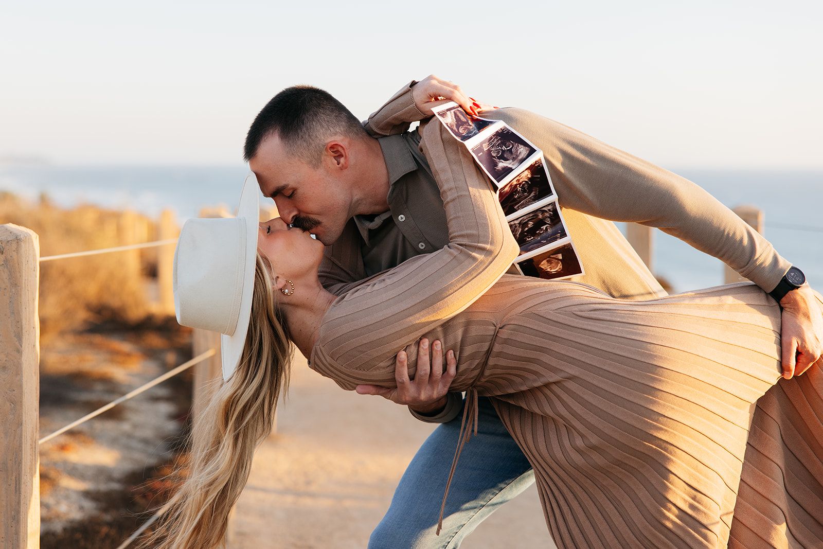 A romantic couple sharing an intimate moment as they embrace in a dramatic dip pose on the beach at sunset.
