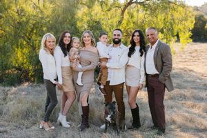 A group in coordinated cream and brown outfits pose together for outdoor family photos in a sunlit field.