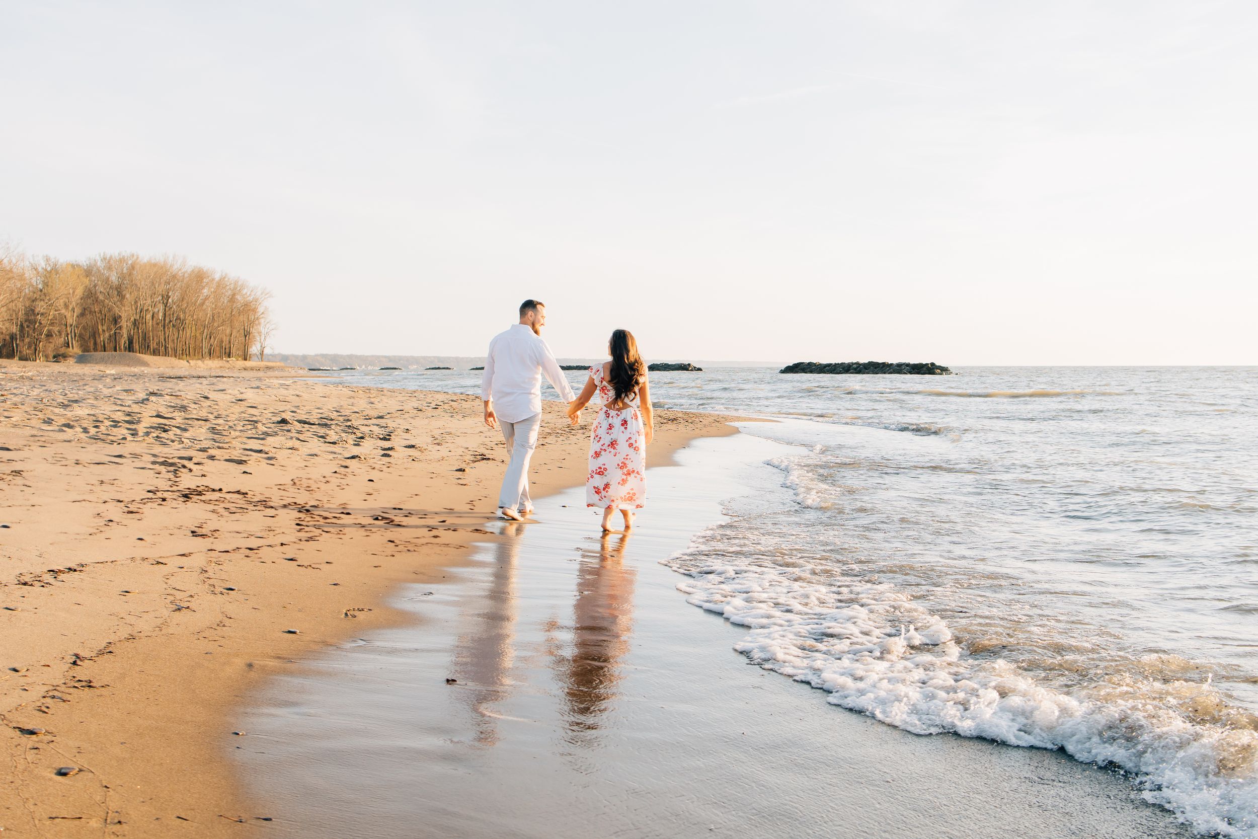 A couple walking hand in hand along a sandy beach at sunset.