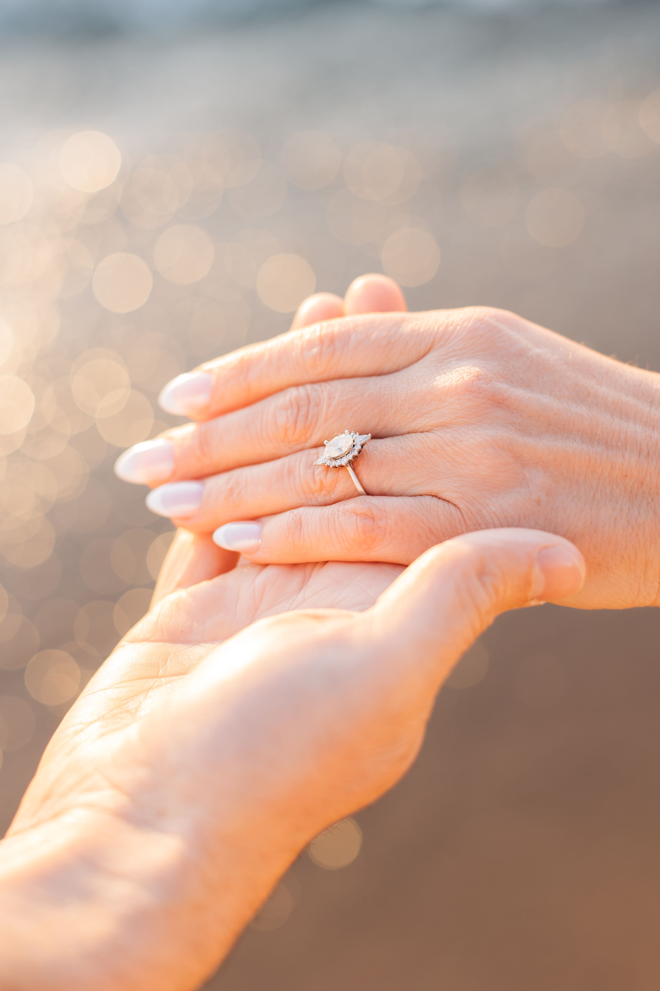 Close-up of hands showing an engagement ring with bokeh light effects in the background.