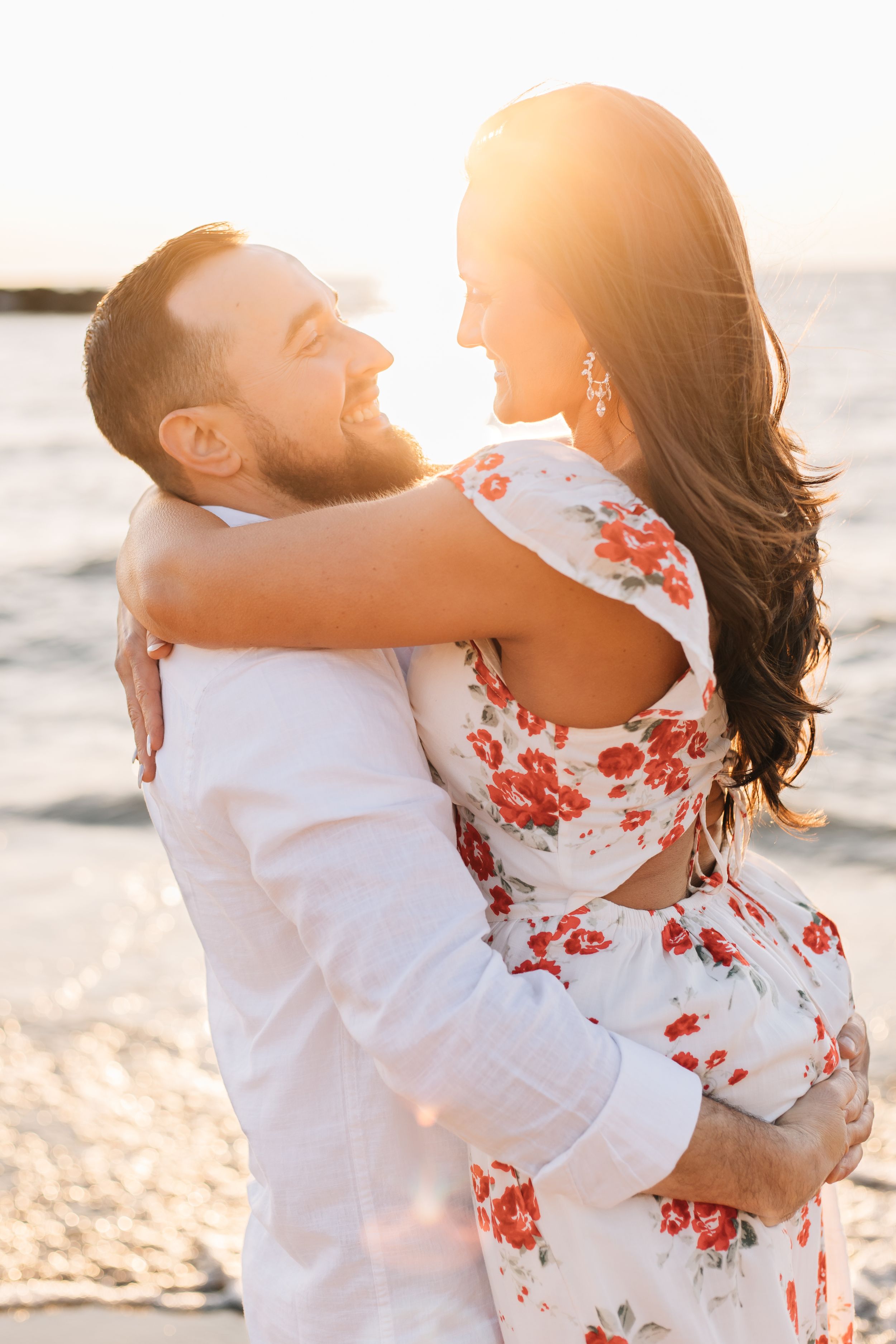 A joyful couple embracing and laughing on the beach at golden hour.