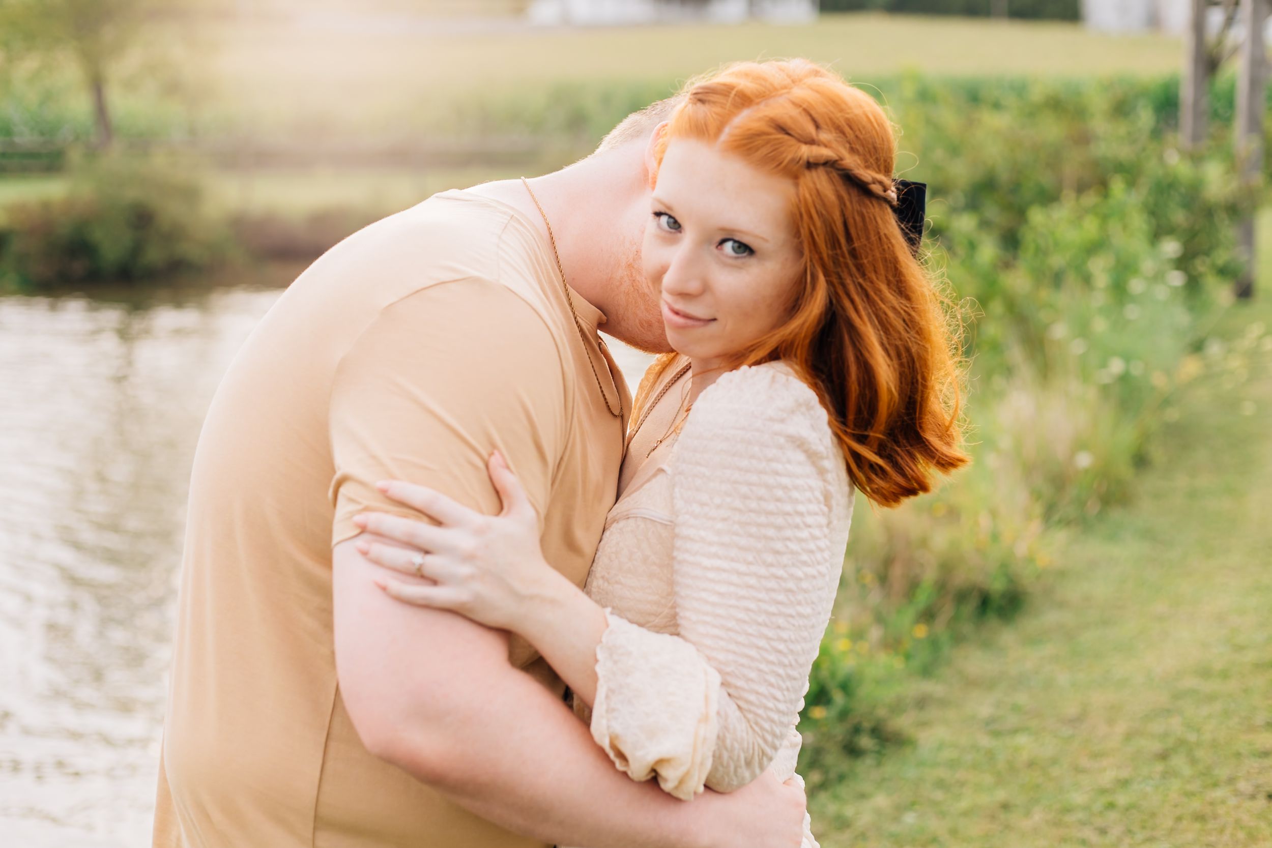 Romantic couple sharing tender embrace outdoors near water at sunset.