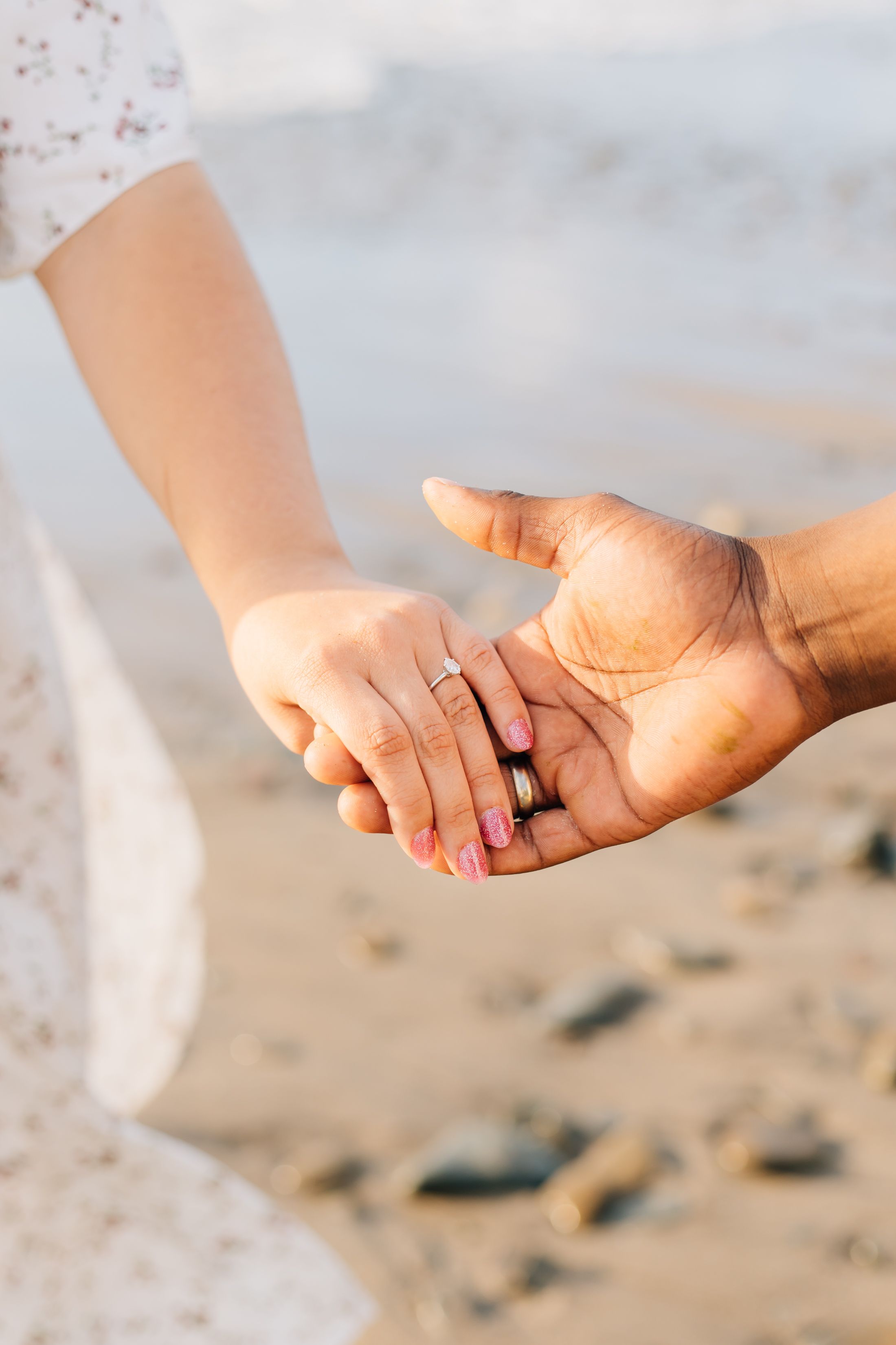 Close-up shots of newlyweds holding hands on a sandy beach, showcasing their wedding rings.