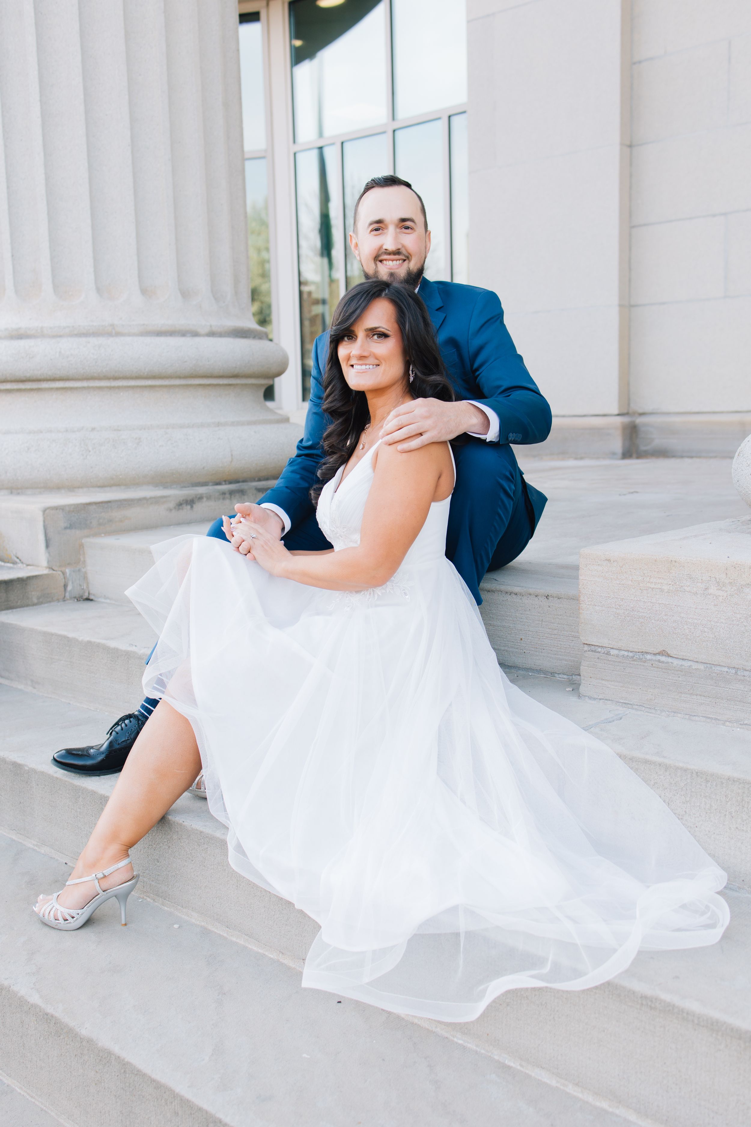 A formal couple posing on marble steps in elegant attire.