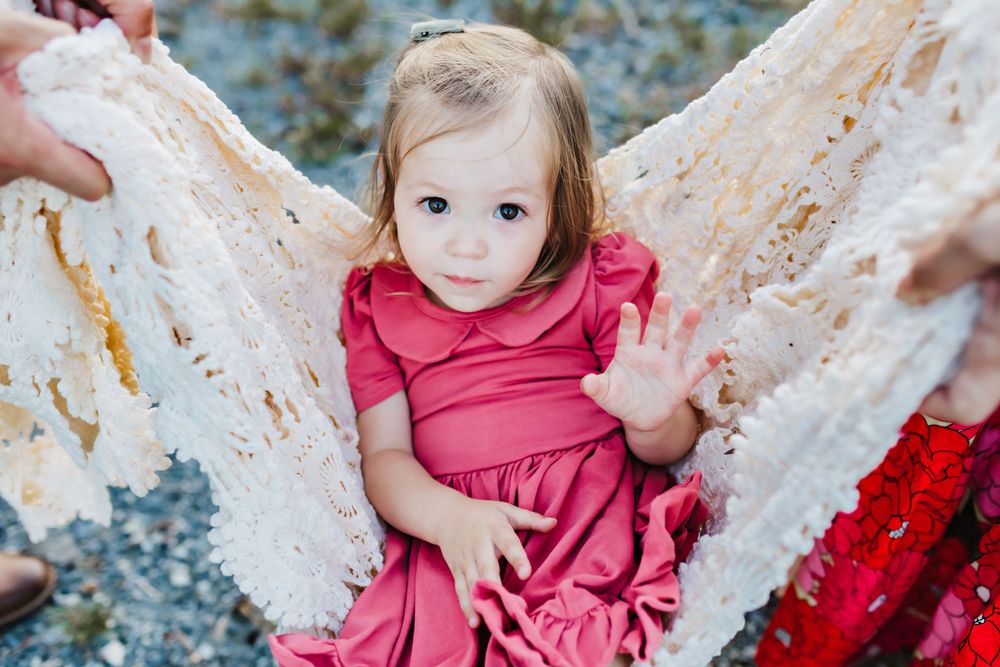 Young child in pink dress sitting between white tree branches outdoors.