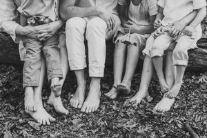 Black and white photo showing a row of barefoot legs and feet of children sitting together on the ground.