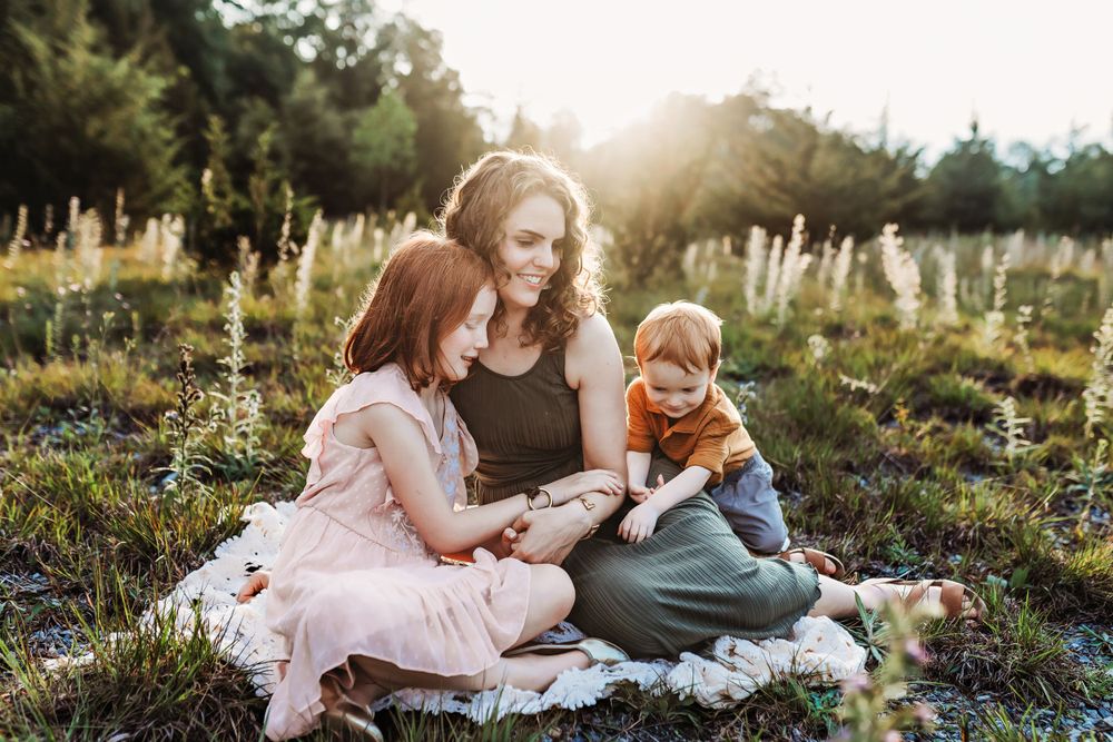People sit together on a blanket in a sunlit meadow during golden hour.