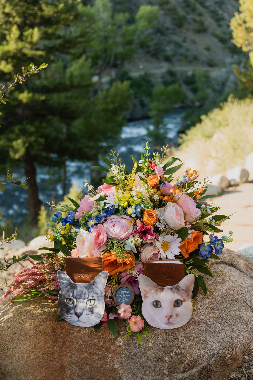 Colorful floral arrangement with pink roses and wildflowers displayed in ceramic cat planters near a river.
