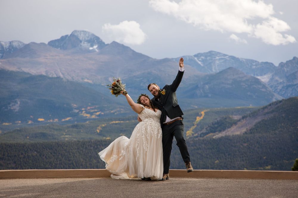 A couple in wedding attire strike a joyful pose against a backdrop of majestic Rocky Mountains in Colorado.