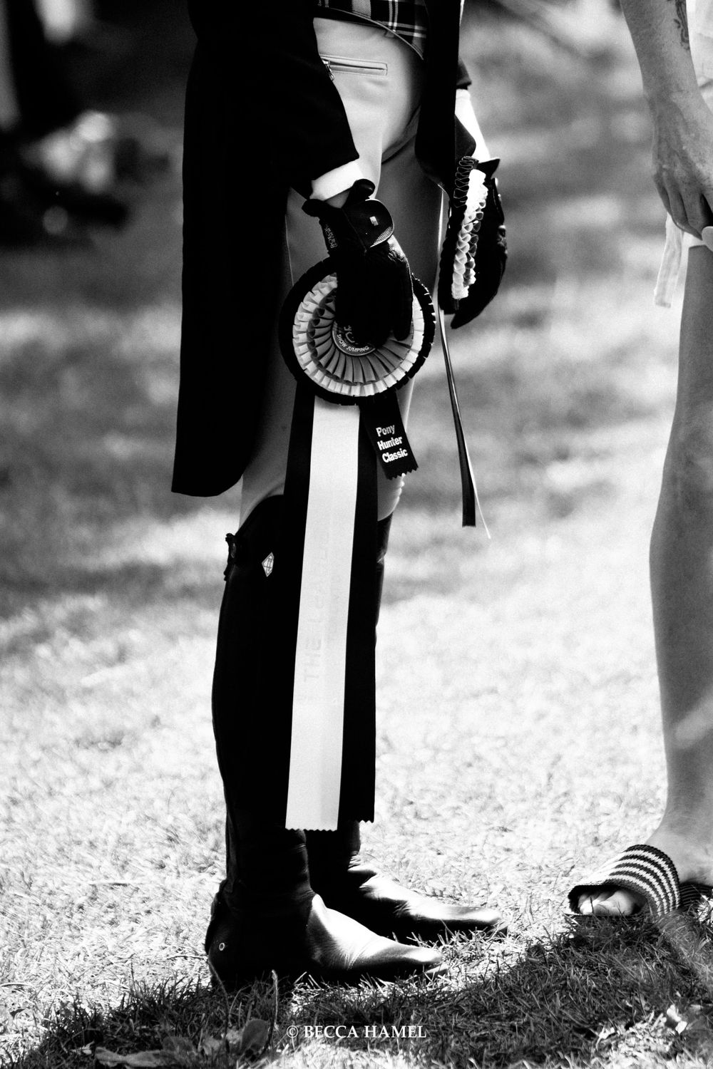 A black and white close-up of equestrian show ribbons and boots.
