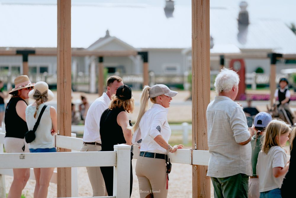 Spectators gather at a wooden railing to watch an equestrian event.