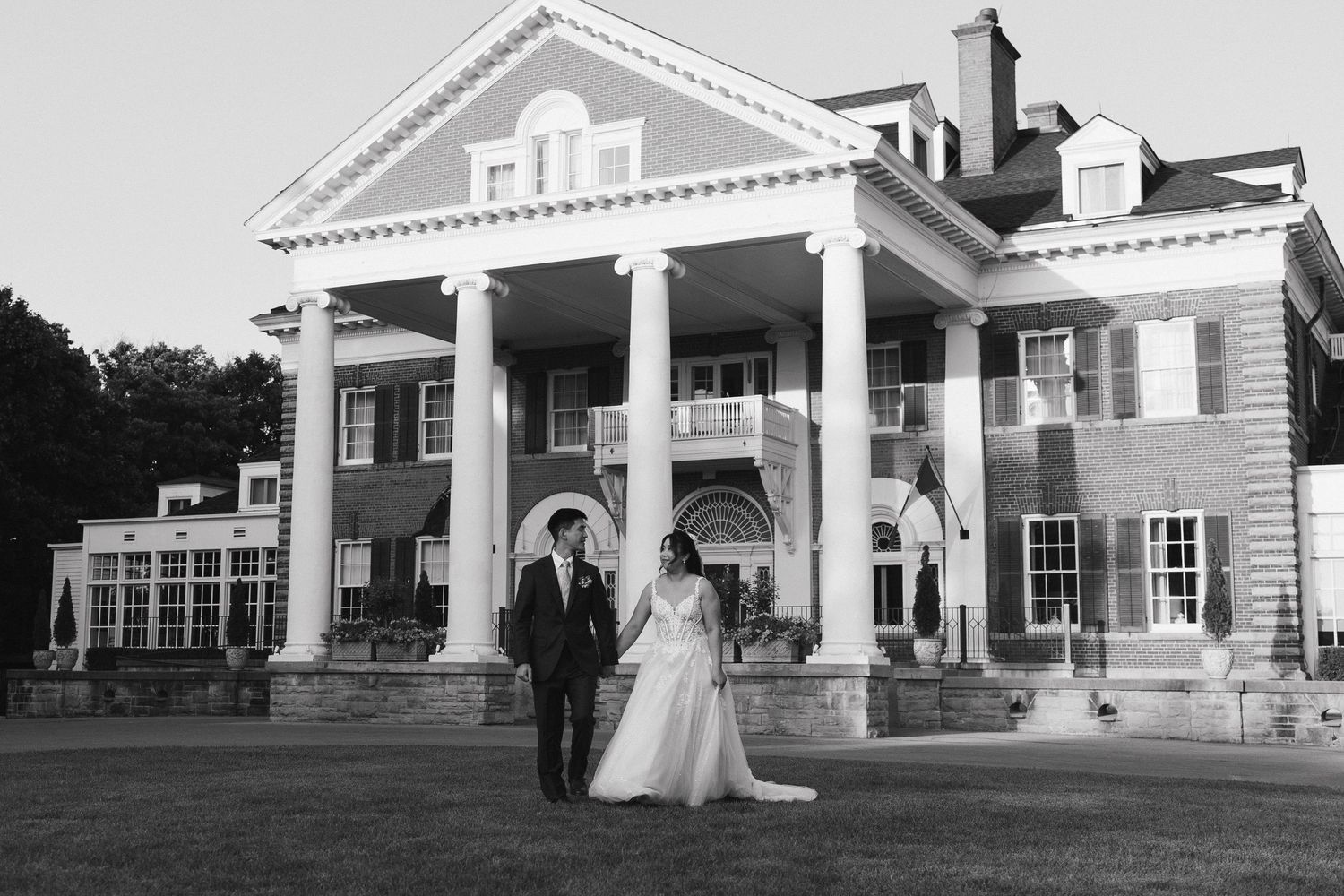 A newlywed couple walking away from Langdon Hall hand in hand in black and white