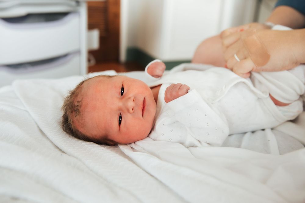 Alert newborn baby in white clothing lying on white bedding. fresh48. Newport hospital