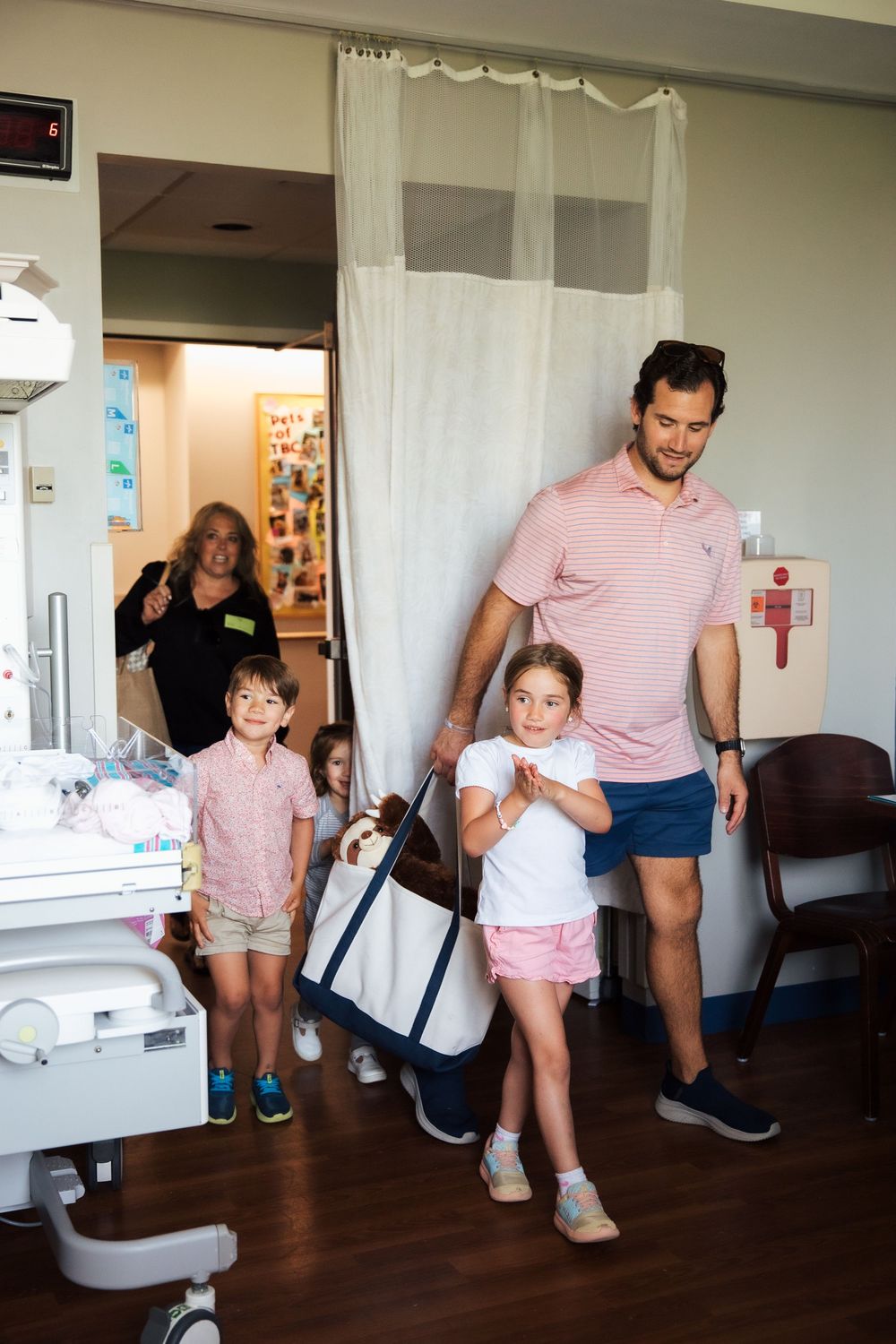 Family with children entering a hospital room to meet a new baby, father in pink polo shirt leading kids through curtain. fresh 48, Newport