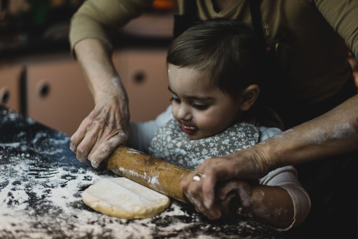 nieta estirando masa con palo de amasar y las manos de su abuela ayudándola a sostener el palo