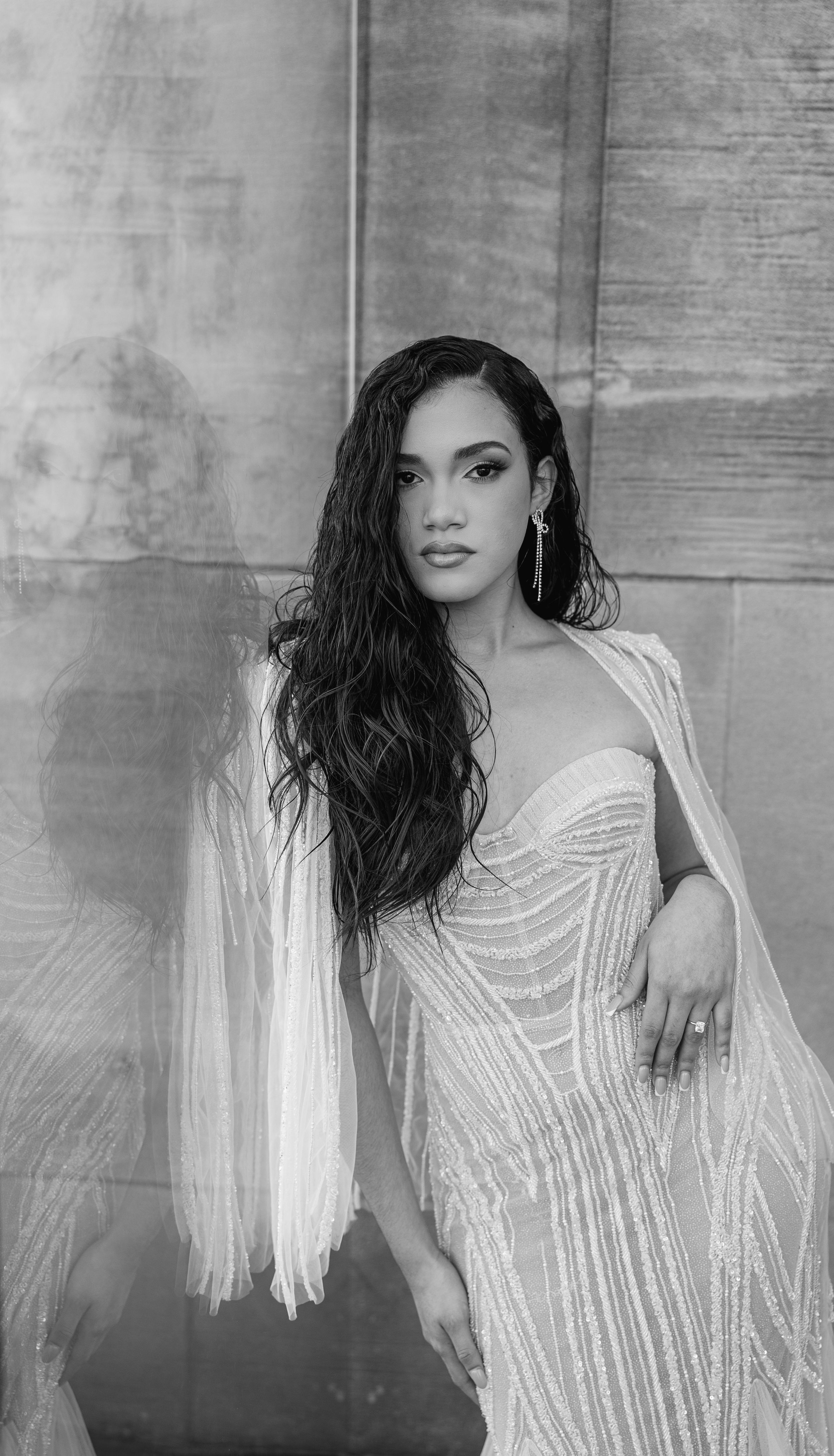 Black and white portrait featuring a woman in a beaded gown with flowing sheer sleeves and long wavy hair.
