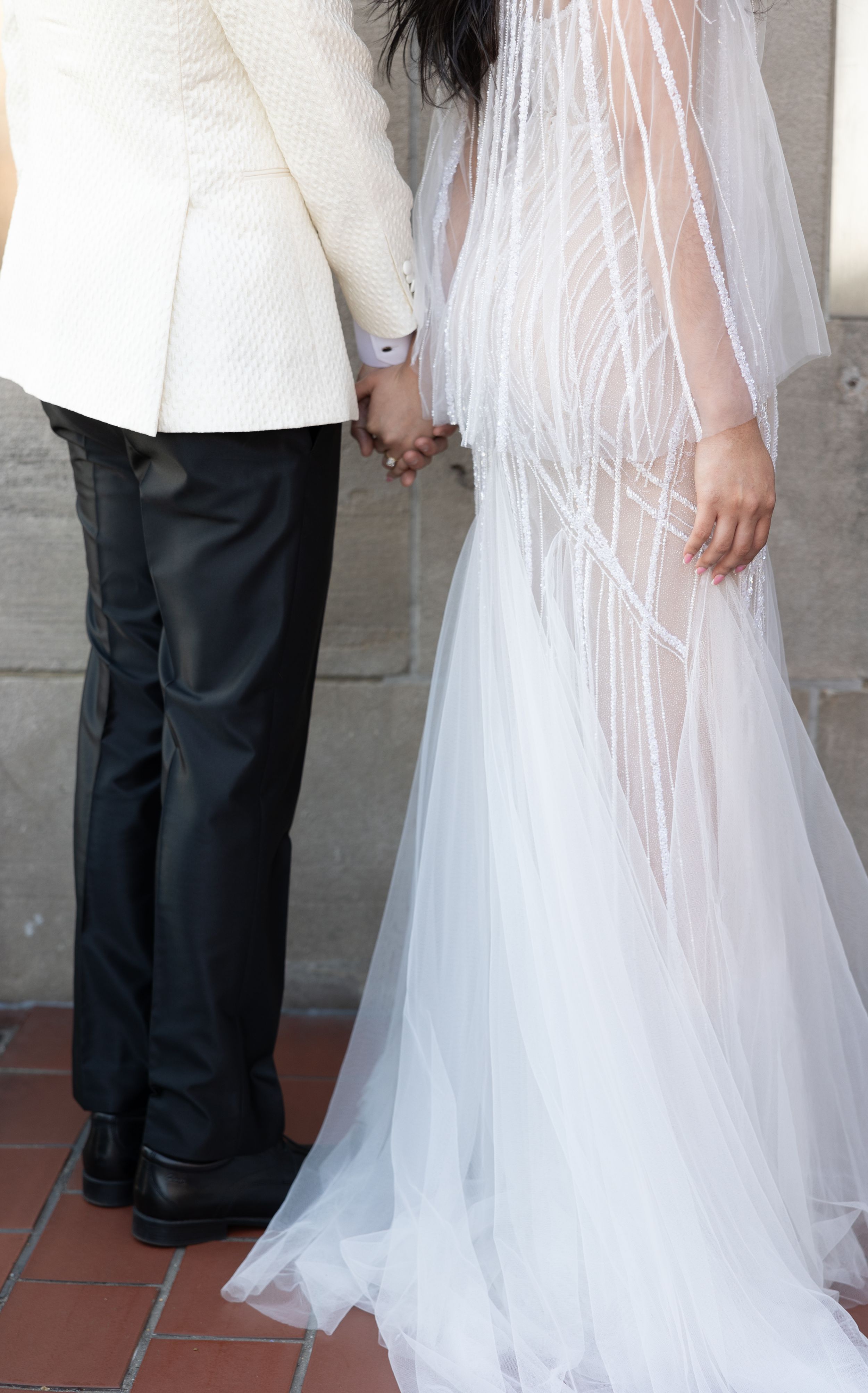 Side view of couple holding hands, showcasing white wedding dress and formal suit details.