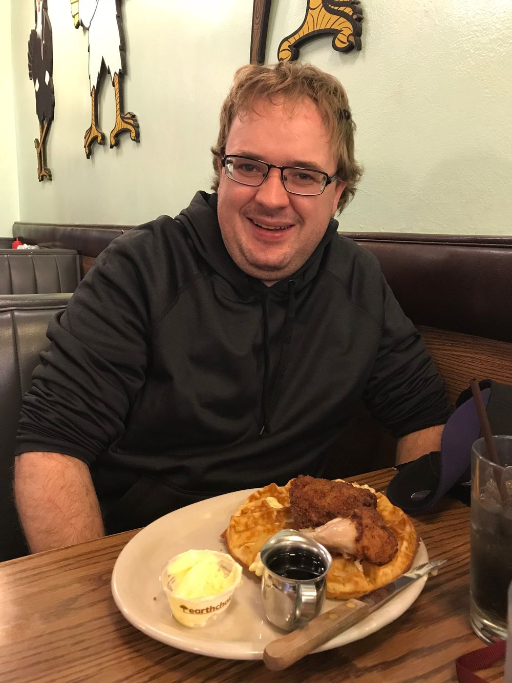 Diner patron seated in a restaurant booth with chicken and waffles plate and condiments on the table.