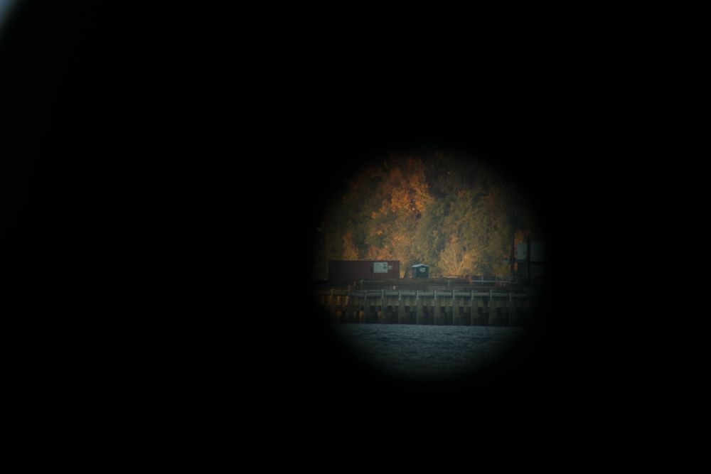 Dark circular view through a telescope or viewfinder showing a distant landscape.