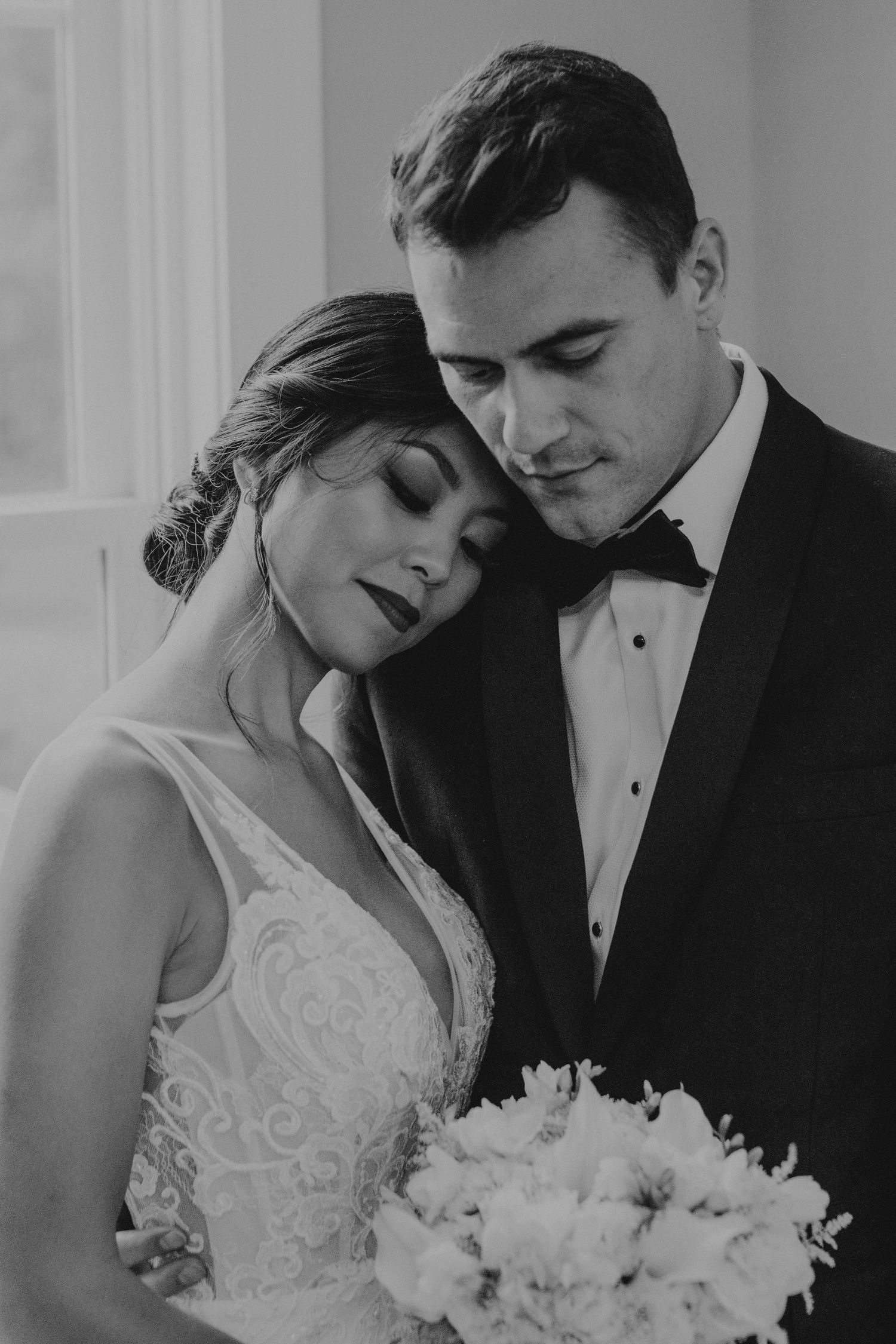Black and white wedding portrait with couple embracing while bride holds white floral bouquet.
