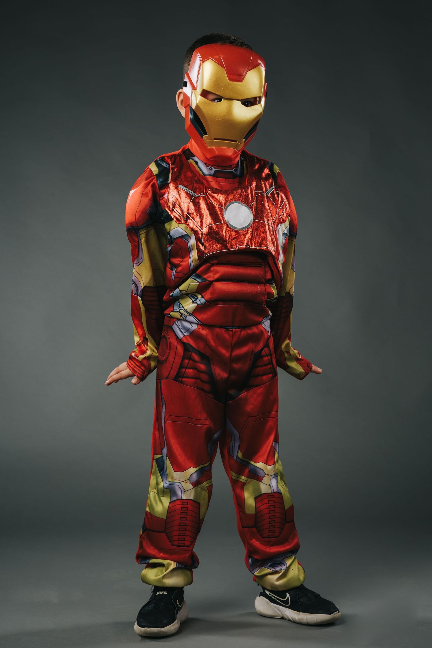Child wearing Iron Man costume posing against dark background.