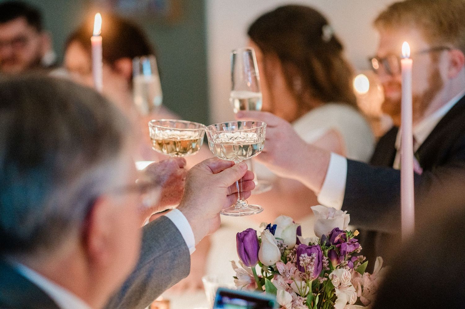 Wedding guests raise champagne glasses in a candlelit toast during an elegant reception celebration.