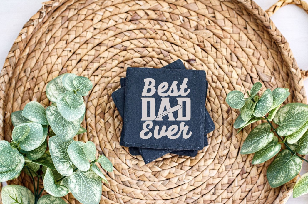 Best Dad Ever text on navy blue tag displayed on woven jute mat with artificial green leaves.
