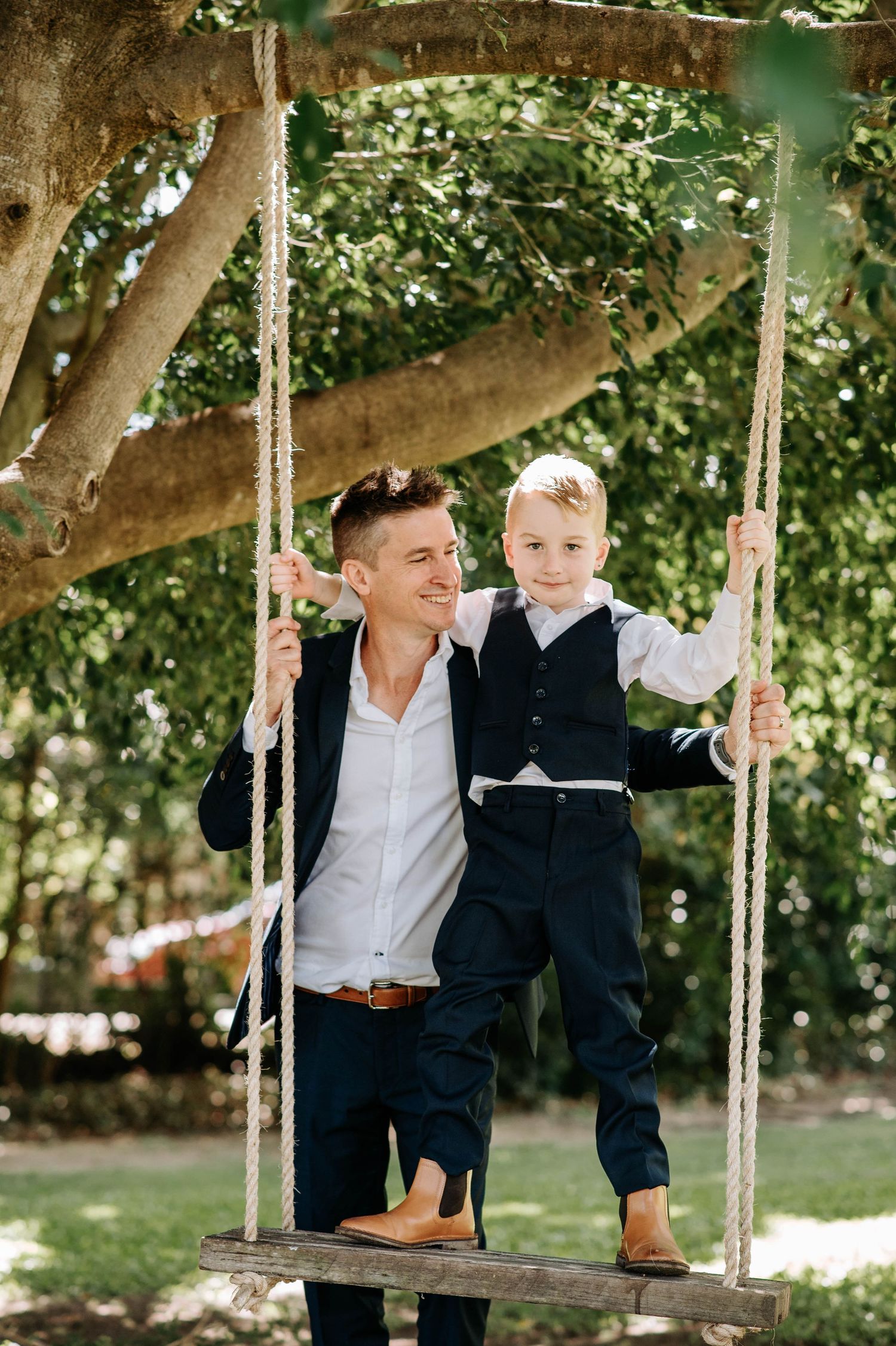 A playful moment shared on a wooden swing hanging from a large tree.