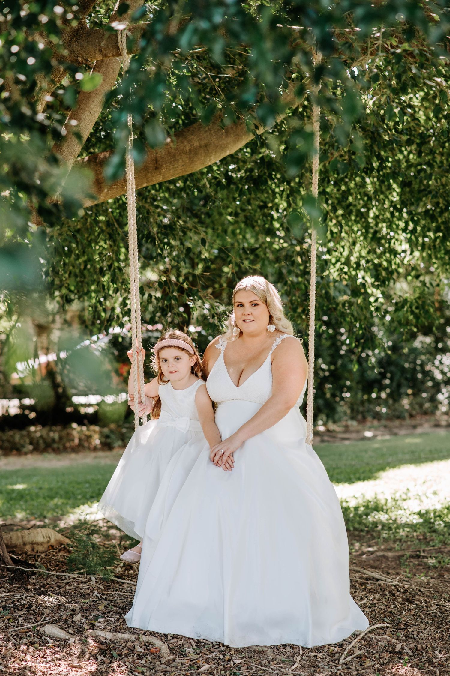 Two people in white dresses posing together on a garden swing.