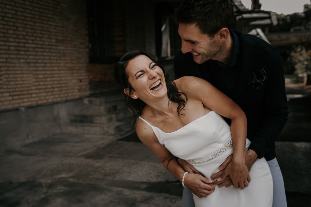 Groom hugging laughing bride in white dress during outdoor wedding photo session.