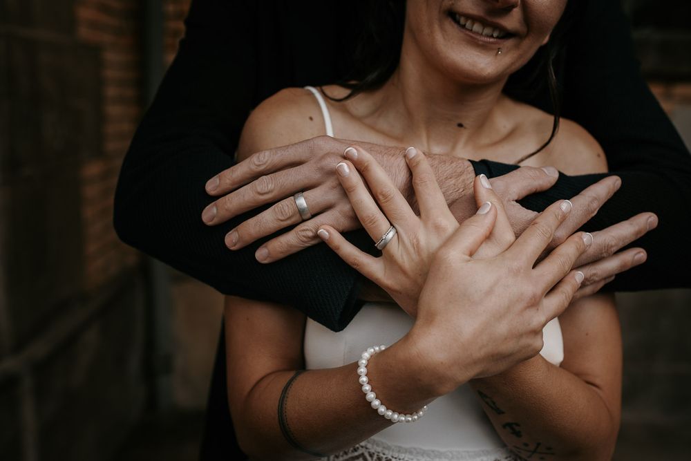 Close-up of bride and groom hands intertwined showing wedding rings and pearl bracelet.