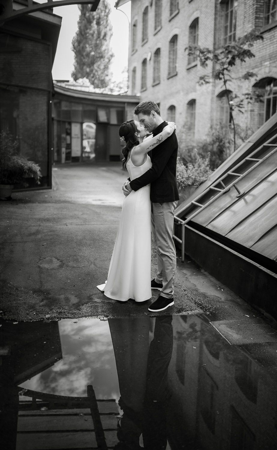 Black and white photo of bride and groom embracing with puddle reflection below.