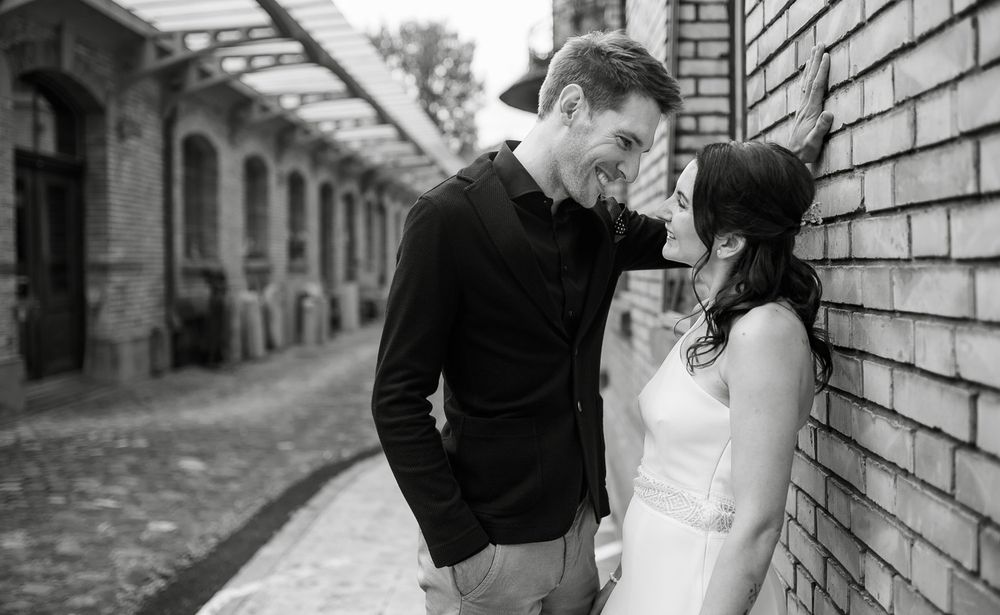 Black and white photo of smiling couple sharing tender moment against brick wall.