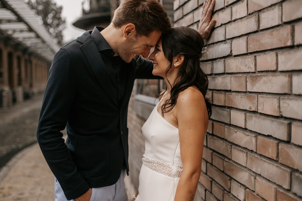 Couple sharing intimate forehead-to-forehead moment against rustic brick wall outdoors.