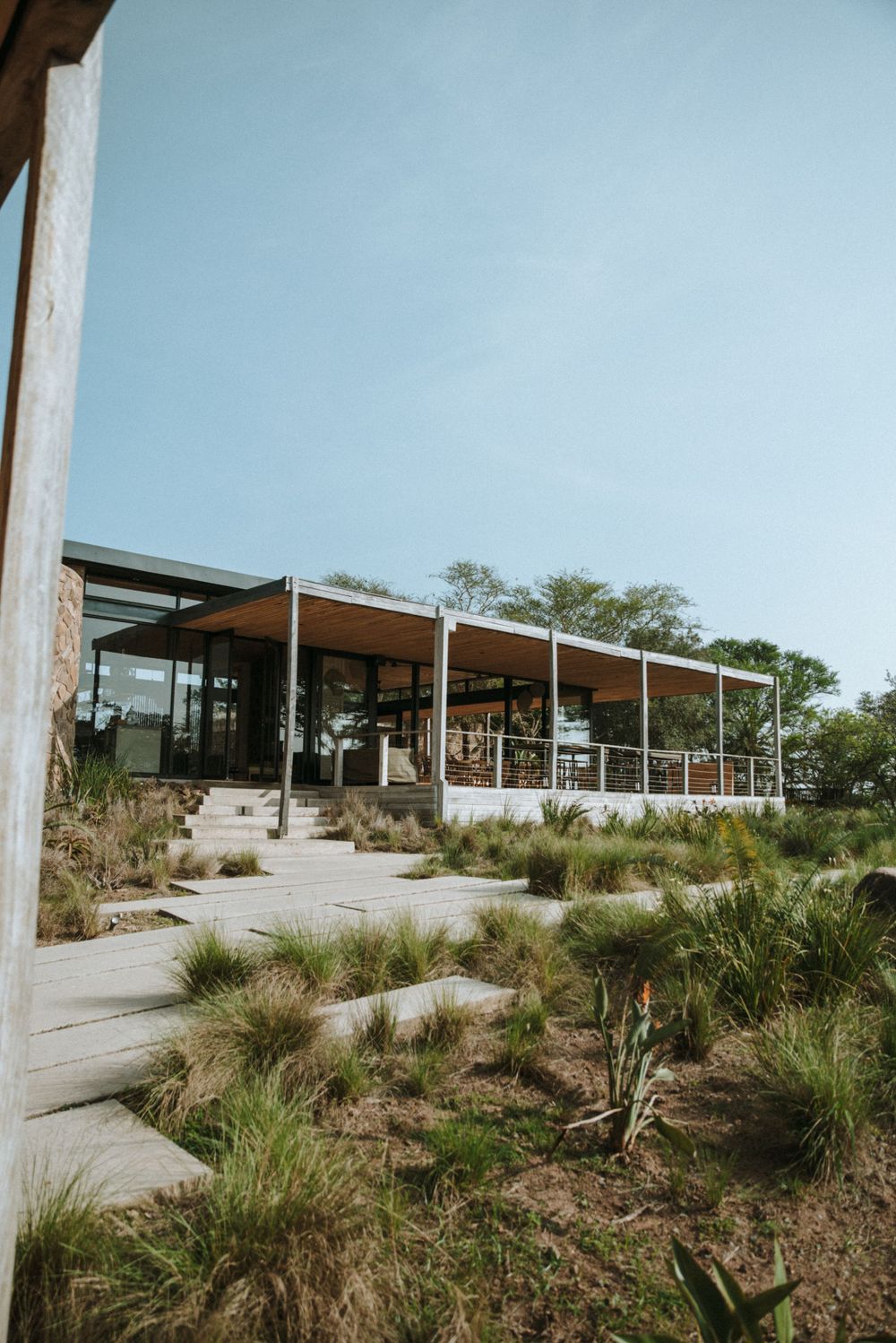 Modern outdoor venue with glass walls and natural landscaping against a blue sky.