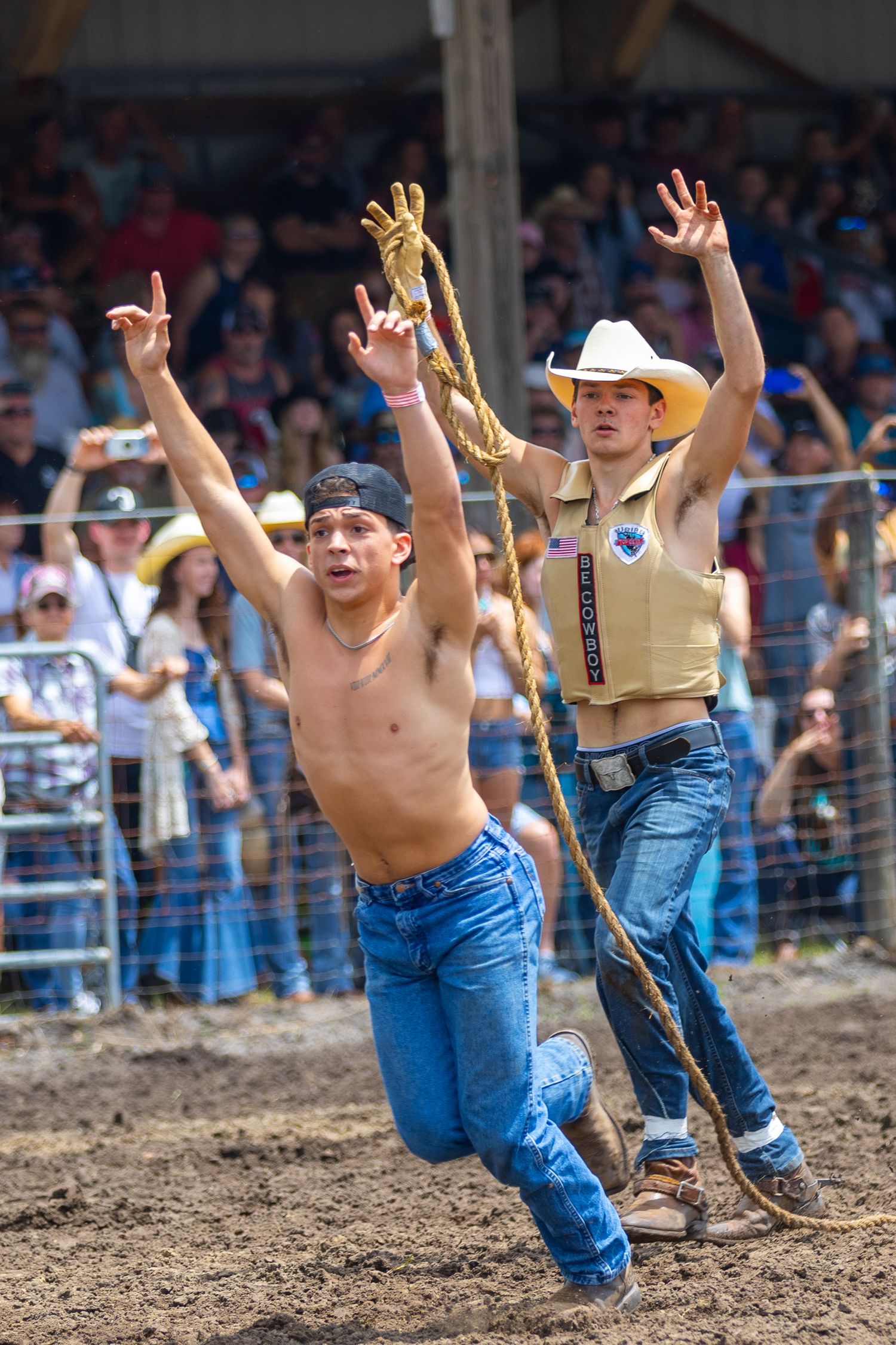 Two rodeo competitors celebrating with raised arms in front of crowd. Deland, Florida